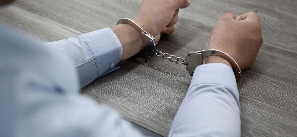 Selective focus shot of male hands in handcuffs on a wooden table